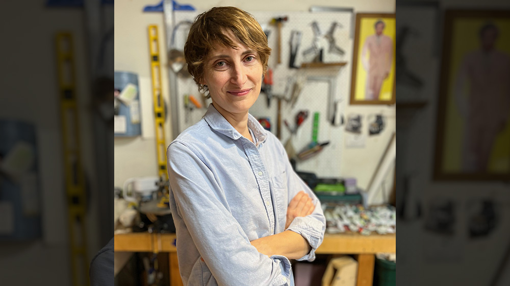 Betsy Odom stands smiling in front of a wall of art supplies.